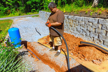 Plumber stands connect to water well working with black hose while digging in ground for plumbing system