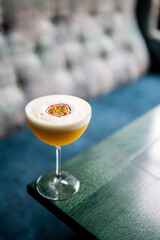 Close-up of a tropical passion fruit cocktail in a glass on a wooden table, garnished with foam and a fruit slice, with a blurred background. Refreshing summer drink concept