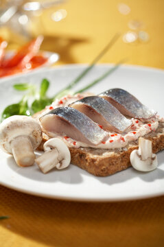 Herring pieces with champignons served on toast on yellow background