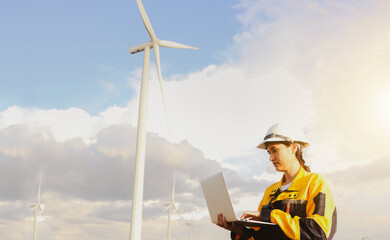 Obraz premium Female engineer holding laptop standing checking rotation function integrity tall tower in wide field wind turbine installation area used generate electricity efficiency and preventive maintenance.