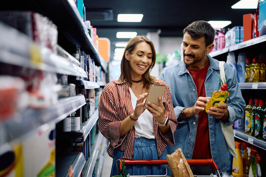 Happy couple using smart phone while buying in a supermarket.