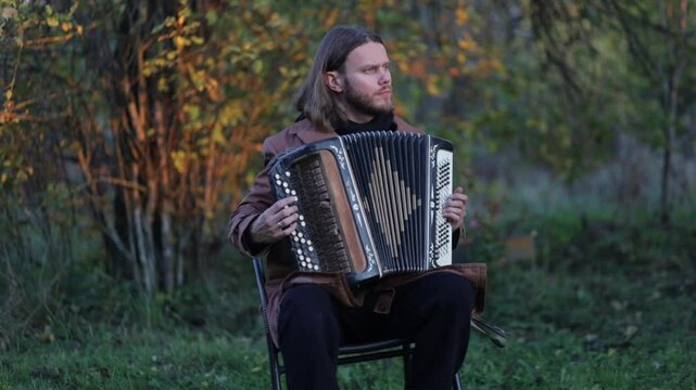 A long-haired man plays the accordion outdoors