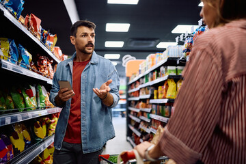 Mid adult man talking to his wife while shopping in supermarket.
