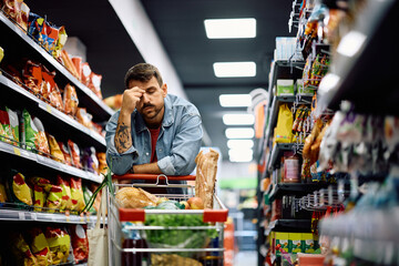 Worried man holding his head in pain while buying in supermarket.