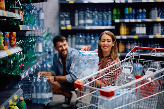 Happy woman buying bottles of drinking water with her husband at the store.