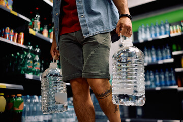 Close up of man buying drinking water plastic bottles in supermarket.