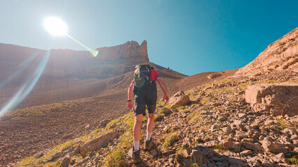 Climbing to the Agujas de Lavasar in Aragon, a mountaineer advances along a rocky path surrounded by large peaks, enjoying breathtaking views of the Ibon de Lavasar in the Pyrenees.
