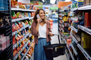 Happy woman communicating on cell phone while buying in supermarket.