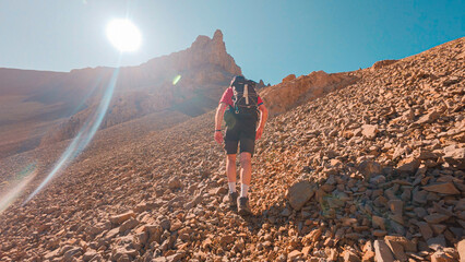 Mountaineer in full ascent to the Agujas de Lavasar, in the Aragon Pyrenees, surrounded by imposing rock formations and mountains, with the Ibon de Lavasar shining in the background.
