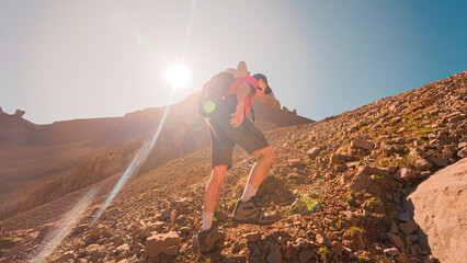 On the way to the Agujas de Lavasar in the Aragon Pyrenees, a mountaineer traverses a rocky terrain, surrounded by giant mountains and the crystal blue Ibon de Lavasar.
