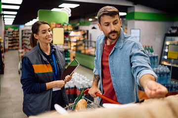 Happy supermarket worker talking to her customer at the store.