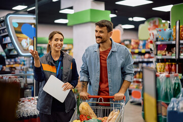 Happy man talking to female manager while buying in supermarket.