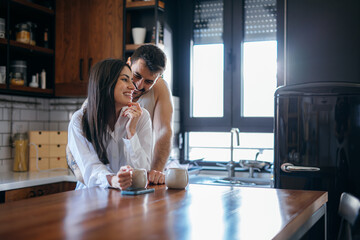 Young couple sharing a tender moment while drinking coffee in their modern kitchen, enjoying the morning light