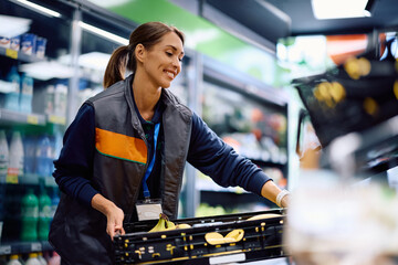 Happy female worker at fresh fruit section in a supermarket.