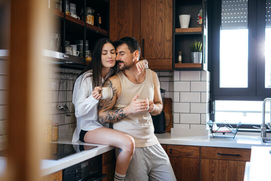 Young loving couple embracing and drinking coffee in modern kitchen, enjoying intimacy and sharing a tender moment together