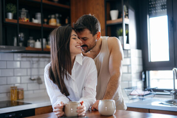 Happy couple enjoying breakfast together in a modern kitchen, sharing smiles and affection over steaming mugs of coffee