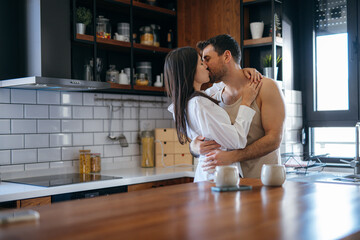 Young couple sharing a passionate kiss and warm embrace in a stylish kitchen, savoring a tender moment of love and connection together