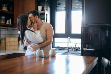 Young couple kissing in a modern kitchen, enjoying a romantic moment while preparing breakfast