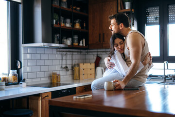 Young couple embracing in a modern kitchen, sharing a tender moment filled with love and warmth while enjoying their morning coffee together