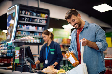 Happy man packing groceries in a bag at supermarket checkout.