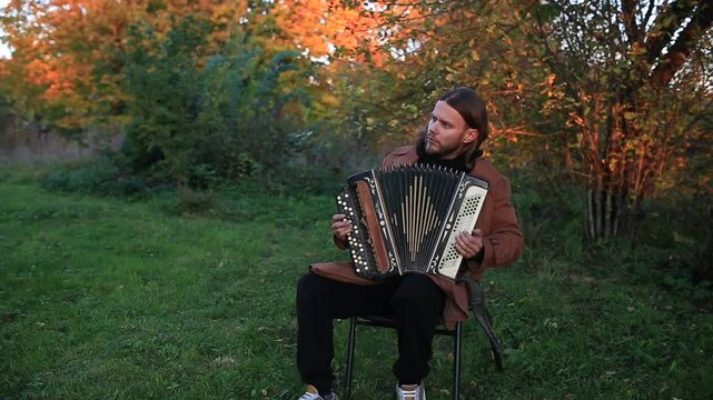 A long-haired man plays the accordion outdoors