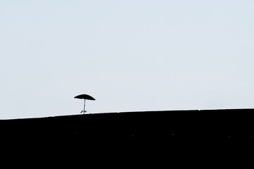 A lone umbrella is silhouetted against a pale sky, standing on a dark, undefined horizon. The image...