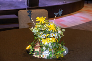  A whimsical table centerpiece features yellow and white flowers, adorned with fairy and dragon...