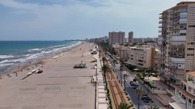 Mucha Vista beach meets crashing surf, lined with palm trees, tall buildings, and a coastal road