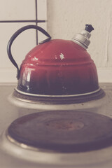 Antique red kettle resting on stovetop, waiting for water to boil as morning light streams through...