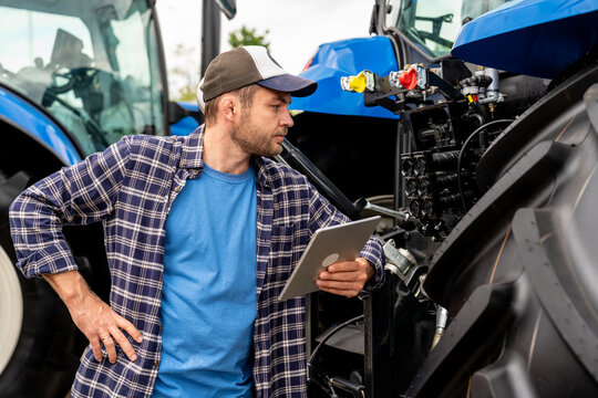 Farmer with tablet inspecting new tractor at agricultural equipment dealership - Powered by Adobe