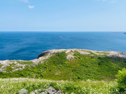 Scenic view from Signal Hill in St. John&rsquo;s, Newfoundland, with green coastal cliffs, Atlantic Ocean, walking trails, and a ship offshore.