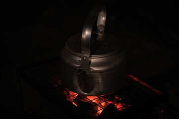 Aluminum campfire camping kettle boils on coals at night on a tourist grill in nature