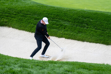 A golfer executes a powerful bunker shot, sending sand and the golf ball flying. This dynamic image...