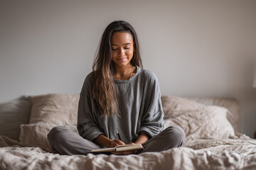 Teen girl journaling on bed in calm room with neutral bedding