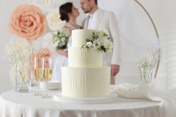 Happy married couple together indoors, focus on wedding cake and glasses of champagne on table