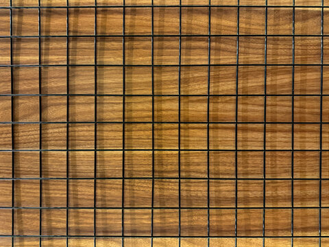 Close up of black wiremesh on top of brown wood panel. Seamless background texture.