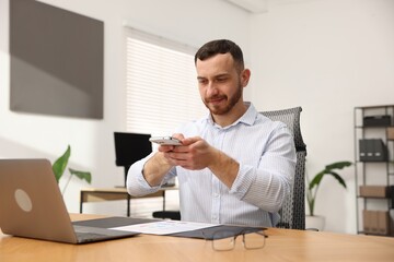 Man taking photo of document using scanning app on smartphone at desk in office