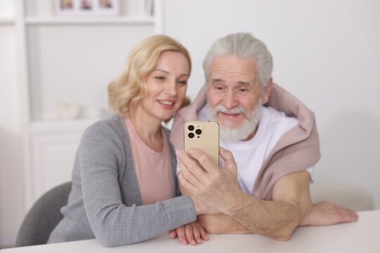 Senior man and mature woman watching something on smartphone at home, selective focus. Happy couple