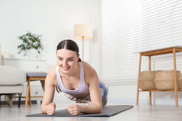 Fototapeta premium Smiling woman in sportswear doing plank exercise at home. Space for text
