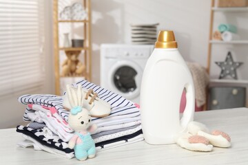 Bottle with fabric softener, baby clothes and toy on light wooden table indoors