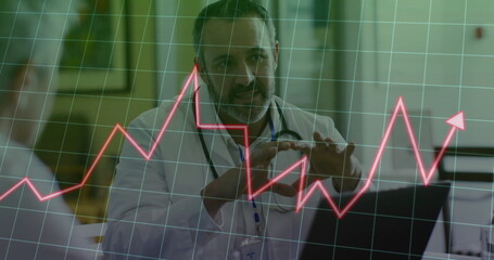 Reviewing doctor in white coat analyzing red data chart on laptop in clinic, with stethoscope