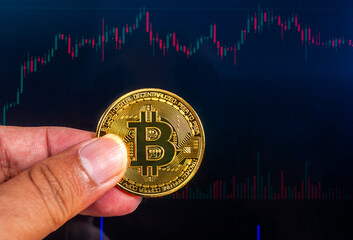 Close up Crypto currency Bit Coin held in fingers, isolated on black background of crypto price fluctuation chart. Crypto money is one of the modern digital exchange tools for today's global society.