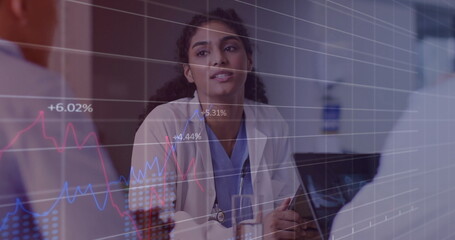 Analyzing data charts, doctor in blue scrubs speaking with colleagues in hospital room, laptop