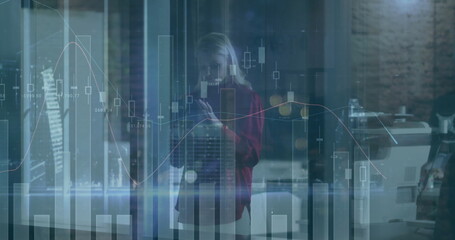 Analyzing financial charts on glass panel in office, wearing red blazer with smartphone near copier