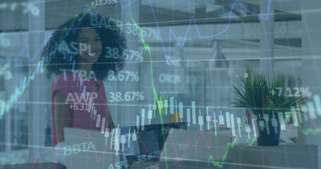 Smiling businesswoman holding laptop in modern open-plan office, with stock market chart overlays
