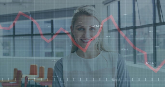 Standing professional in blazer showing data in modern office with grid windows, red graph overlay