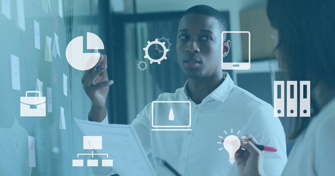 Man and woman brainstorming in office, with glass board markers, document, notes and floating icons
