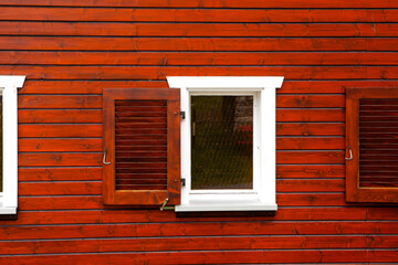Open window with shutters on a burgundy wooden house.


