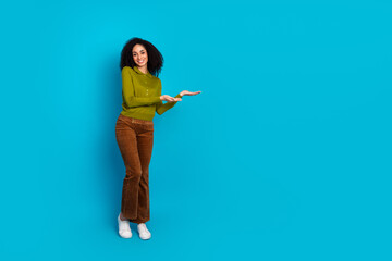 Young smiling woman in casual fashion making hand gestures against solid blue background showcasing...
