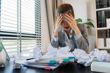 Asian businesswoman stressed holding crumpled paper while working with laptop and documents in...